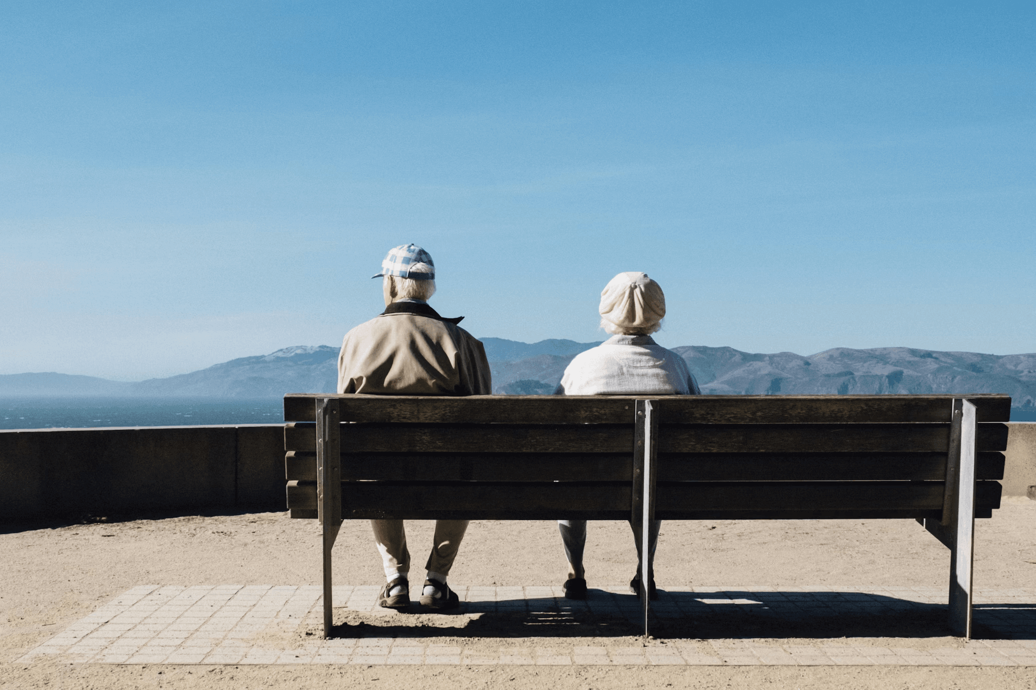Two seniors sitting on a bench looking at the mountains
