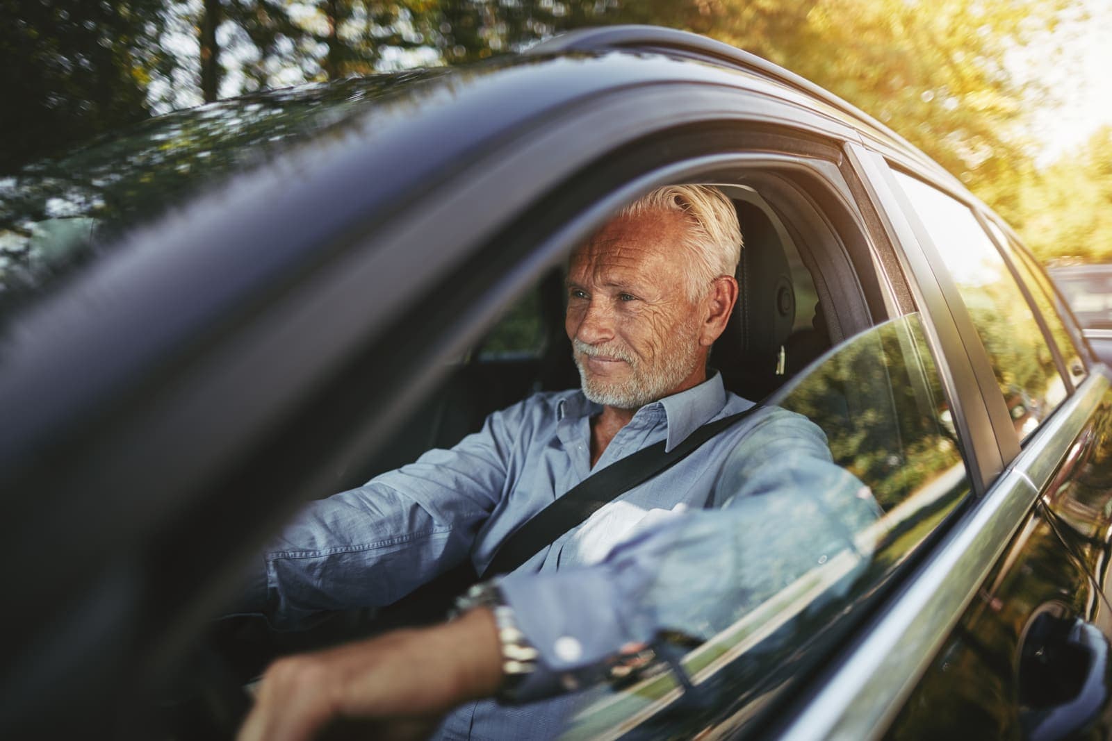 A smiling older man driving on a tree-lined road
